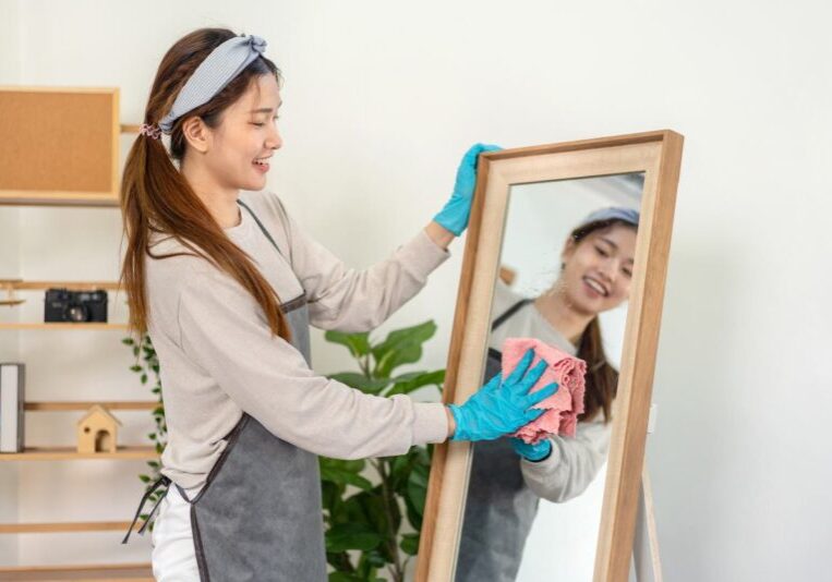 Housekeeper is wearing protective gloves and using microfiber cloth to cleanups and wiping dirt on the glass Housekeeper is wearing protective gloves and using microfiber cloth to cleanups and wiping dirt on the glass while working to perform routine house cleaning.