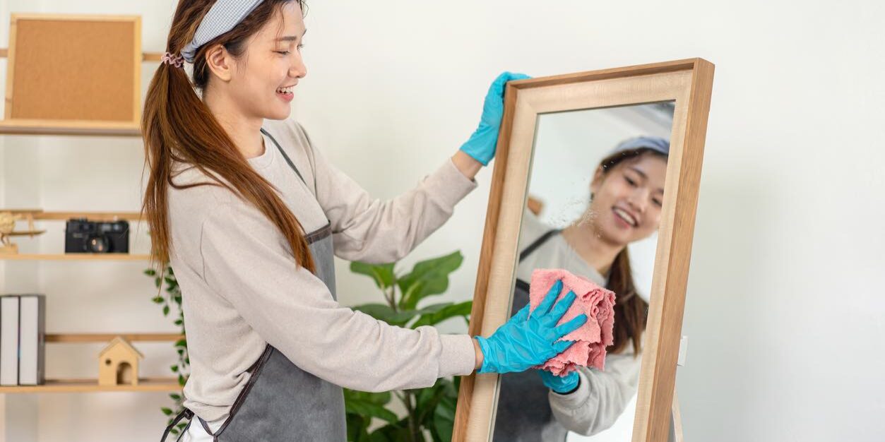 Housekeeper is wearing protective gloves and using microfiber cloth to cleanups and wiping dirt on the glass while working to perform routine house cleaning.