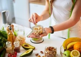 Young happy woman eating different nuts (cashew, hazelnut, almond) in modern kitchen. Healthy food and Dieting concept. Loosing Weight