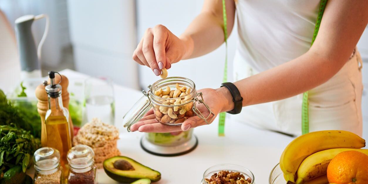 Young happy woman eating different nuts (cashew, hazelnut, almond) in modern kitchen. Healthy food and Dieting concept. Loosing Weight