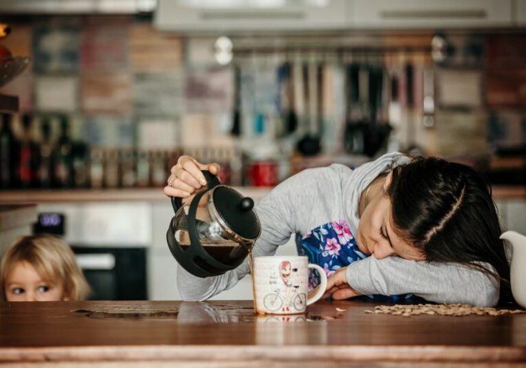 Tired mother, trying to pour coffee in the morning. Woman lying on kitchen table after sleepless night, trying to drink coffee
