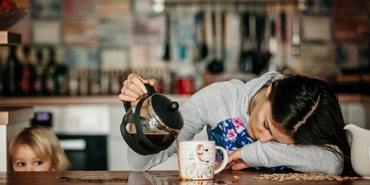 Tired mother, trying to pour coffee in the morning. Woman lying on kitchen table after sleepless night, trying to drink coffee
