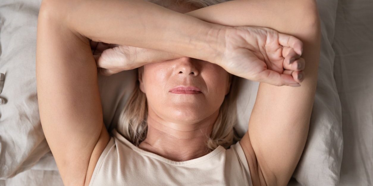 Sleepless mature woman suffering from insomnia close up, lying in bed, older female covering eyes with hands, trying to sleep, nightmares or depression, feeling headache or migraine