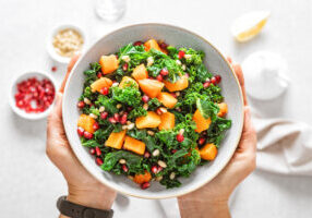 Vegetable salad bowl in woman hands. Fresh kale and baked pumpkin salad. Healthy eating concept