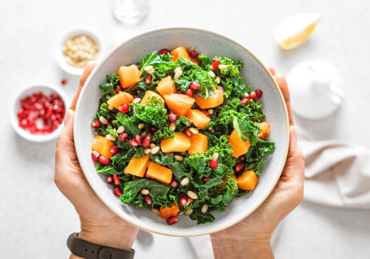 Vegetable salad bowl in woman hands. Fresh kale and baked pumpkin salad. Healthy eating concept