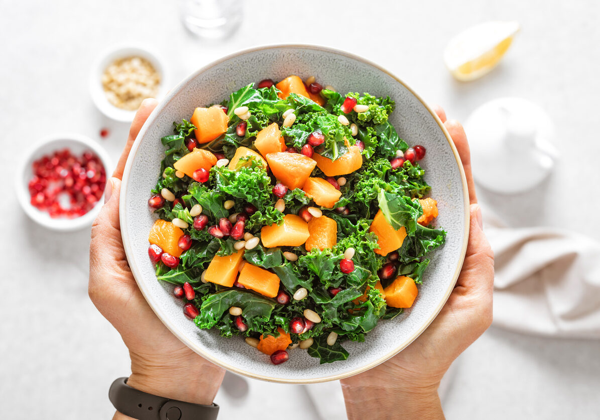 Vegetable salad bowl in woman hands. Fresh kale and baked pumpkin salad. Healthy eating concept