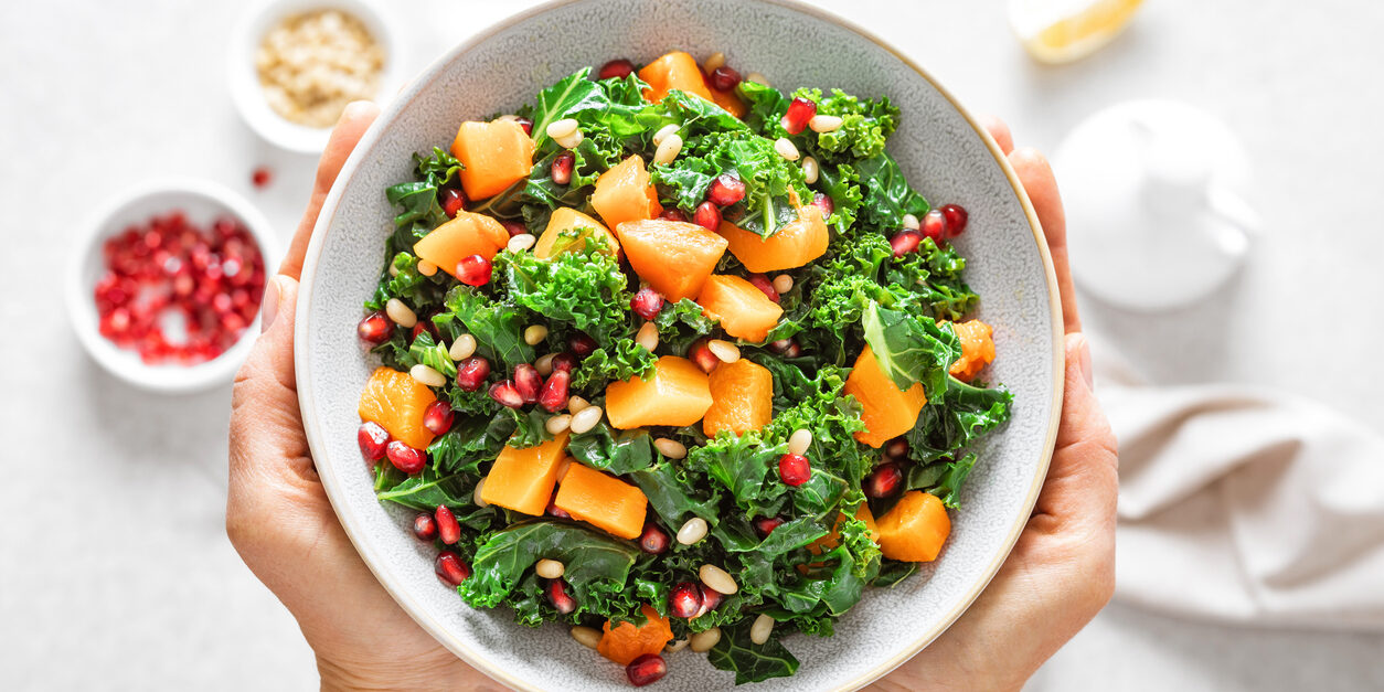 Vegetable salad bowl in woman hands. Fresh kale and baked pumpkin salad. Healthy eating concept