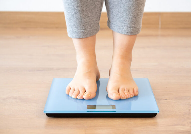 Closeup of a young woman weighing herself on a scale at home