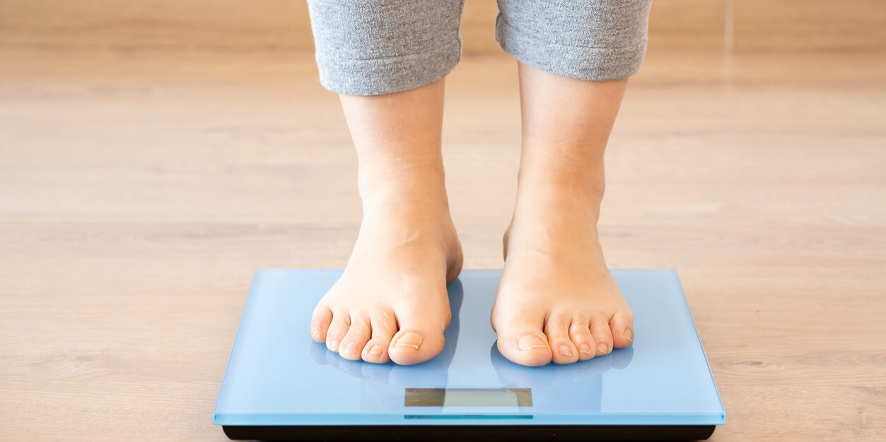 Closeup of a young woman weighing herself on a scale at home
